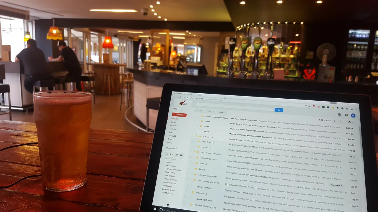 Patrick's laptop and a pint of beer on a wooden bar table, inbox open.